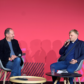 Hendrik Simon und Philippe Sands im Gespräch auf einer Bühne. Links sitzt Philippe Sands und hört zu, rechts spricht Hendrik Simon in ein Mikrofon