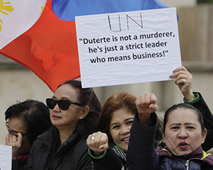 Philippinische Frauen auf einer Demonstration. Eine hält ein Plakat mit der Aufschrift "UN "Duterte is not a murderer, he's just a strict leader who means business!"" hoch