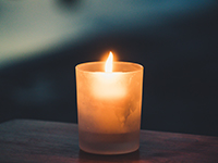 Eine entzündete Kerze steht auf einem Holzbalken.