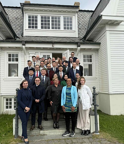 A group of formally dressed people stands in front of a white house