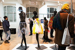 Mannequins wear unusual clothes, some of which are made of plastic. Visitors look at them.