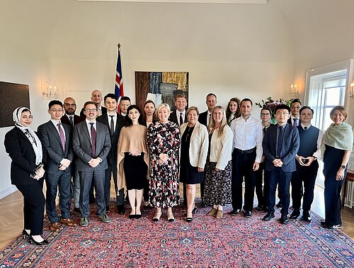 A group of formally dressed people stand in a half circle and in a big room on a fancy rug
