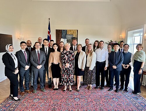 A group of formally dressed people stand in a half circle and in a big room on a fancy rug