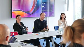 Nicole Deitelhoff, Stefan Kroll und eine Teilnehmerin sitzen an einem Konferenztisch