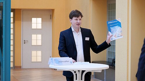 Prof. Malte Göttsche steht an einem Stehtisch und hält ein blaues Buch mit dem Titel CNTR Monitor Perspectives on Dual Use hoch.