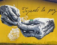 Hauswand mit zwei Händen, die Nadeln halten, und darüber der Schriftzug: "Tejiendo la paz"