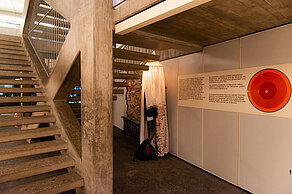 A white fabric is hung under a staircase, which is illuminated from the inside. Next to it is an explanatory panel with text and a circle in various shades of red.