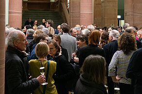 Many people stand in a foyer and talk in small groups.