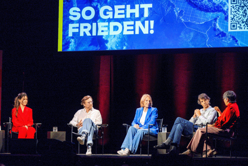 sowie Politikwissenschaftlerin und Polit-Influencerin Nina Poppel (@ninierklärtpolitik), Dokumentarfilmer Carl Gierstorfer, ZDF-Sonderkorrespondentin Katrin Eigendorf, PRIF-Programmbereichsleiter Innerstaatliche Konflikte Jonas Wolff und Moderatorin Shakuntala Banerjee auf der Bühne im Schlachthof Wiesbaden
