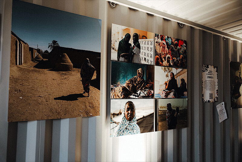 An einer Containerwand hängen Bilder der Fotografieausstellung "Postcards from Khartoum"