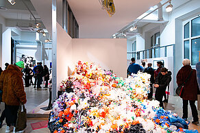 A mountain of garbage is on display in the foreground. Visitors look at works of art in the background.