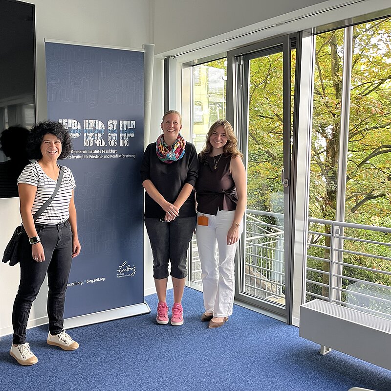 Auf dem Foto sind drei Personen vor einem PRIF-Banner in einem hellen Raum zu sehen. Links vom Banner steht eine der Lehrerinnen, rechts neben dem Banner in der Mitte die andere Lehrerin und ganz rechts Daniela Hobel, Doctoral Researcher am PRIF.