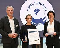 Drei Personen mit Zertifikat vor dem Hintergrund des Total E-Quality Logos