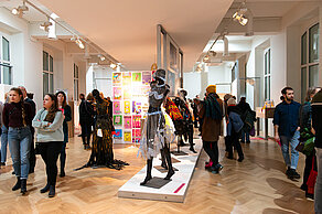 Visitors look at the exhibition. There are mannequins in fancy clothes and a billboard with colorful posters.