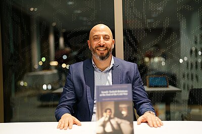 Eldad Ben Aharon is sitting at a table. His book is in front of him.