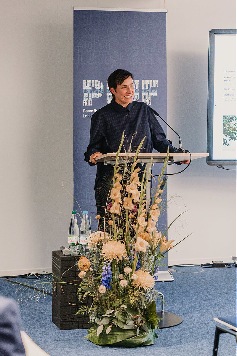 Nicole Deitelhoff steht am mit Blumen geschmückten Redner*innenpult
