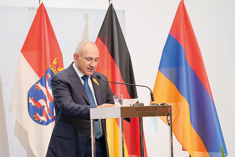 Armenian Prime Minister Nikol Pashinyan stands at the lectern delivering his acceptance speech, with the flags of Hesse, Germany, and Armenia in the background.
