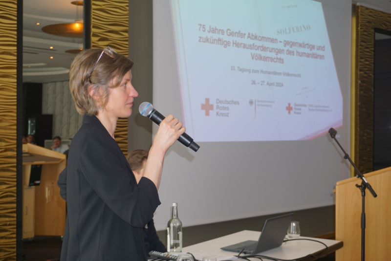 Regine Schwab steht mit einem Mikrofon vor einer Power Point Präsentation