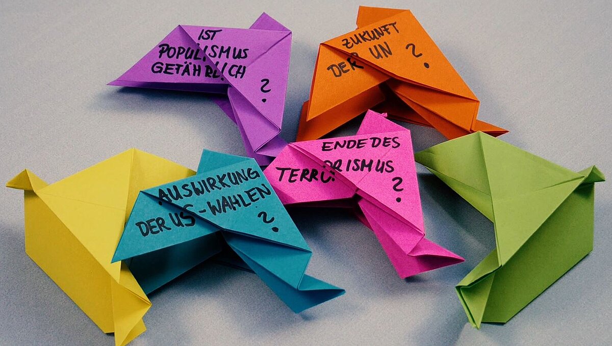 Aus Papier gefaltete bunte Friedenstauben, die mit verschiedenen Fragen beschrieben sind