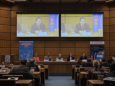 Foto von einem gefüllten Plenarsaal. Auf dem Podium sitzen fünf Menschen. Jan Quosdorf, der auf dem Podium sitzt, ist vergrößert auf zwei Leinwänden im Hintergrund zu sehen.