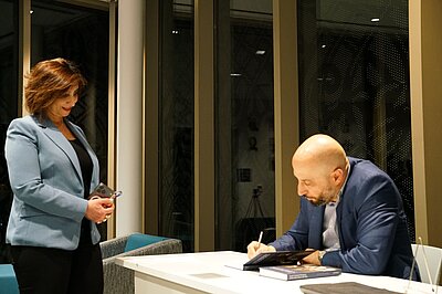 Eldad Ben Aharon is signing one of his books. A woman is standing to his left.