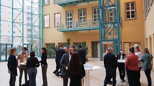 Mehrere Kleingruppen von Menschen stehen an Stehtischen in einem Atrium