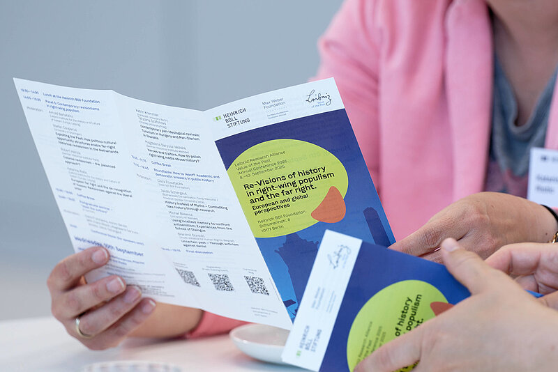 Fotografie von Händen, die einen auseinandergefalteten Flyer der Konferenz halten.